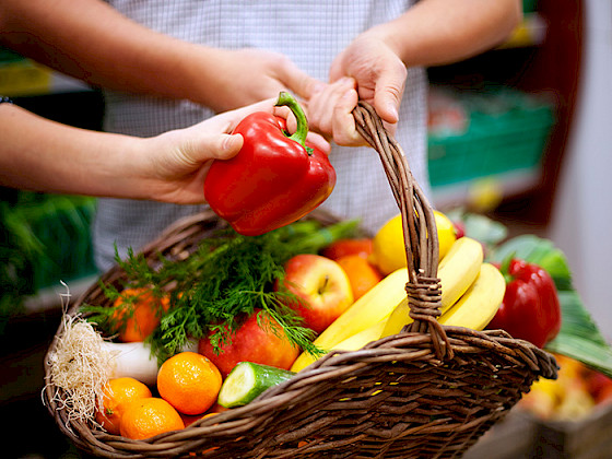 Mano sostiene un pimentón rojo sobre una canasta llena de frutas y verduras.