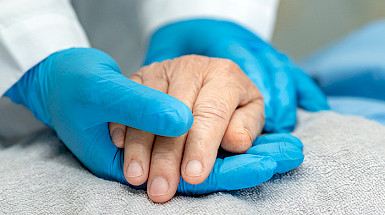 Gloved hand holding a patient’s hand