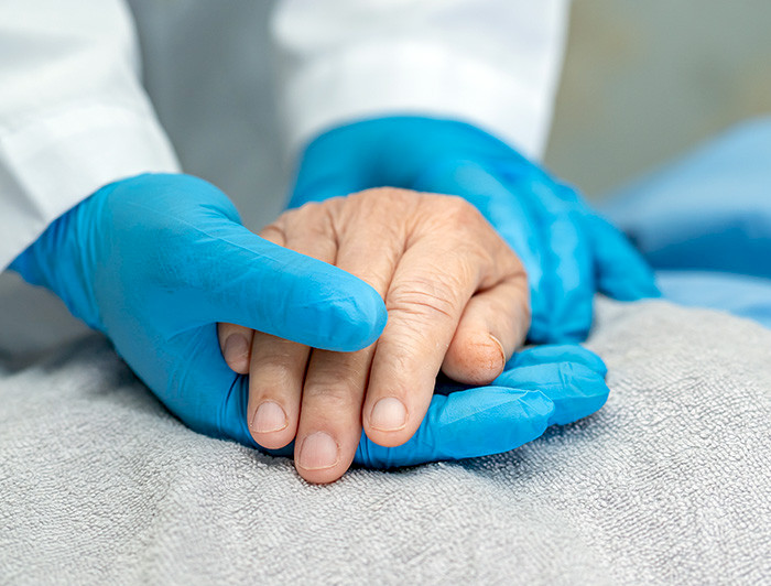 Gloved hand holding a patient’s hand 