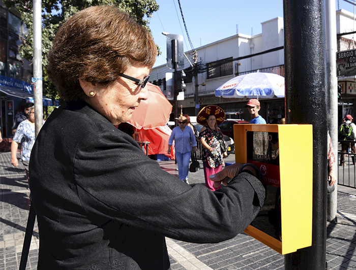 Anciana con un braselete en el brazo extiende la luz roja en un semáforo gracias a una tecnología que este último porta ensamblada. 