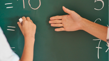 Hands writing numbers on a green chalkboard..