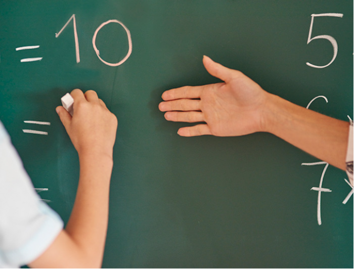 Hands writing numbers on a green chalkboard..