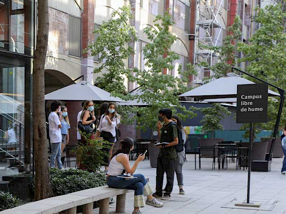 Estudiante en Casa Central cerca de un letrero de Campus Libre de Humo