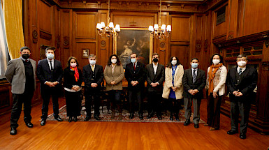 grupo de hombres y mujeres de pie, con mascarilla y ropa formal abrigada