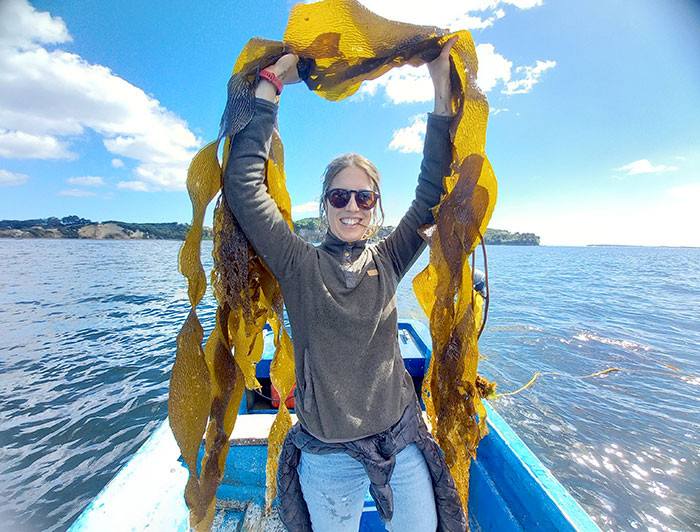 María José de la Fuente de pie sobre un bote levantando algas sobre su cabeza.