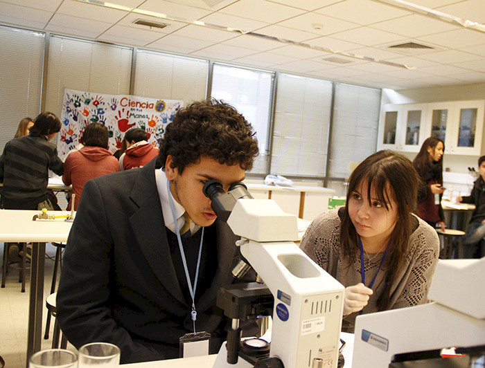 A young man is watching through a microscope, while a woman is supervising him.