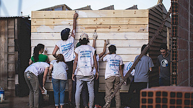 A group of nine young volunteers from Techo are painting white a wall of wood.