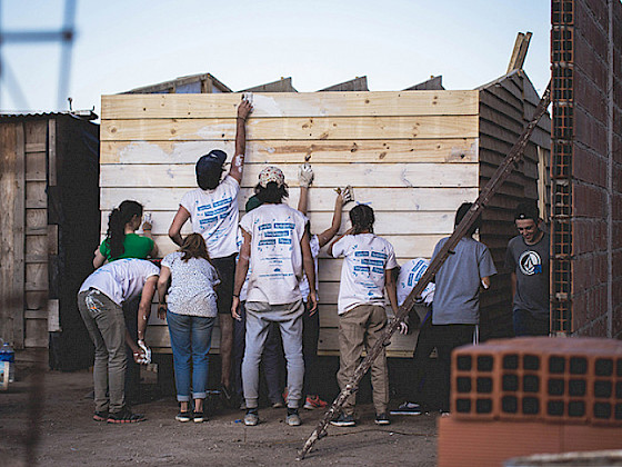 A group of nine young volunteers from Techo are painting white a wall of wood.
