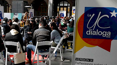 Personas sentadas en sillas conversando junto a un pendón de UC Dialoga.