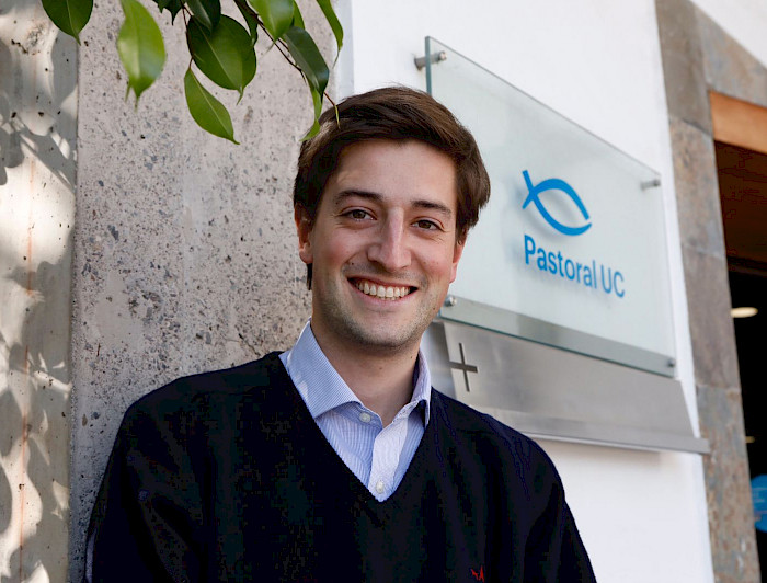 hombre joven sonriendo, detrás suyo hay un letrero que dice Pastoral UC