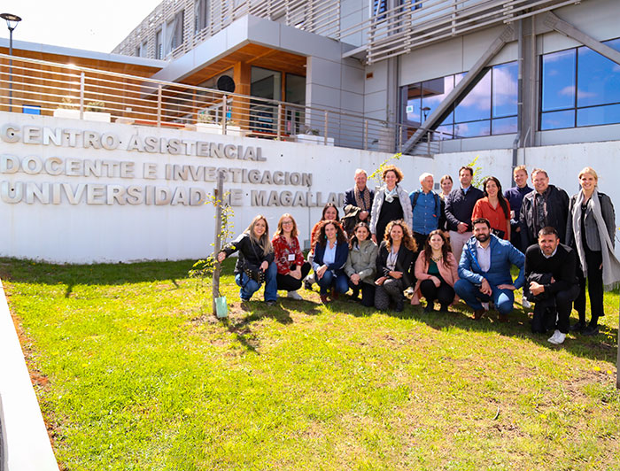 A group of 18 researchers are smiling and posing for the photo in front  of the Teaching and Research Assistance Center in Punta Arenas.