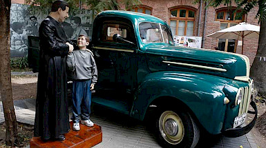 estatua de padre hurtado dándole la mano a un niño, al lado de una camioneta verde