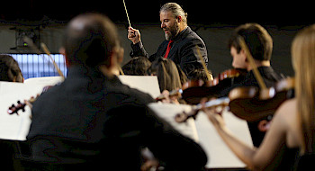Violinistas desenfocados y al fondo el director de orquesta.