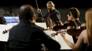 Violinistas desenfocados y al fondo el director de orquesta.