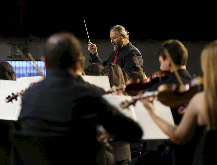 Violinistas desenfocados y al fondo el director de orquesta.