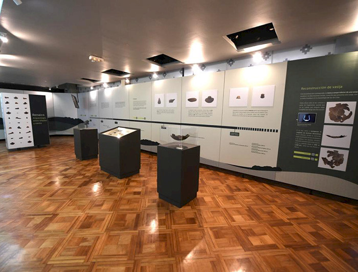The photography shows part of the Renaico exhibit. The wall is in the back with information and images. Above the brown floor are three pillars with ceramic pieces.