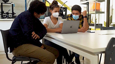 Two young men and one woman are discussing during a manufacturing workshop.