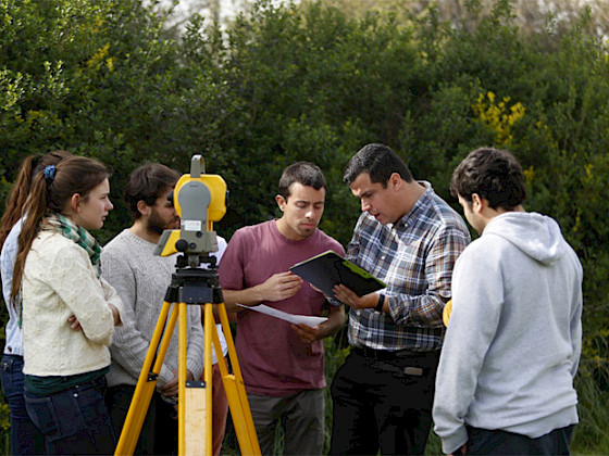 Estudiantes en el exterior, revisando documentos y con apoyo de instrumentos para obras de vialidad