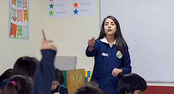 Profesora dando la palabra a una niña con la mano levantada.