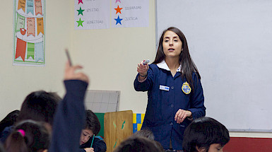 Profesora dando la palabra a una niña con la mano levantada.