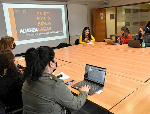 Grupo de académicos en torno a una mesa con una presentación de fondo que dice: "Alianza Lagar, juntos por la Educación Pública Local".