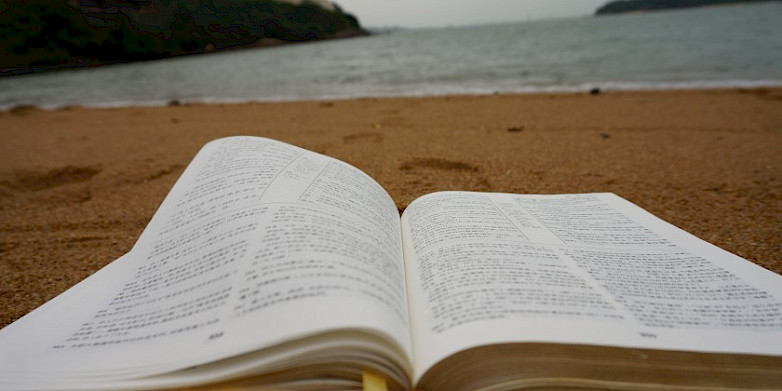 Libro abierto sobre la arena. Al fondo se ve el mar desenfocado.