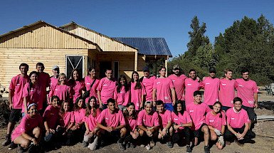 Grupo de jóvenes con poleras rosadas adelante de una casa