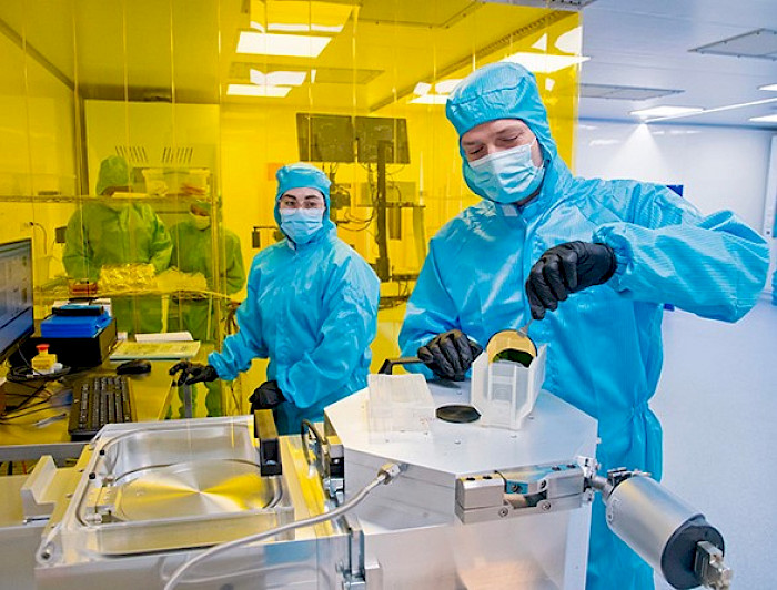 Two scientists wearing masks and blue suits manipulate elements in the laboratory.