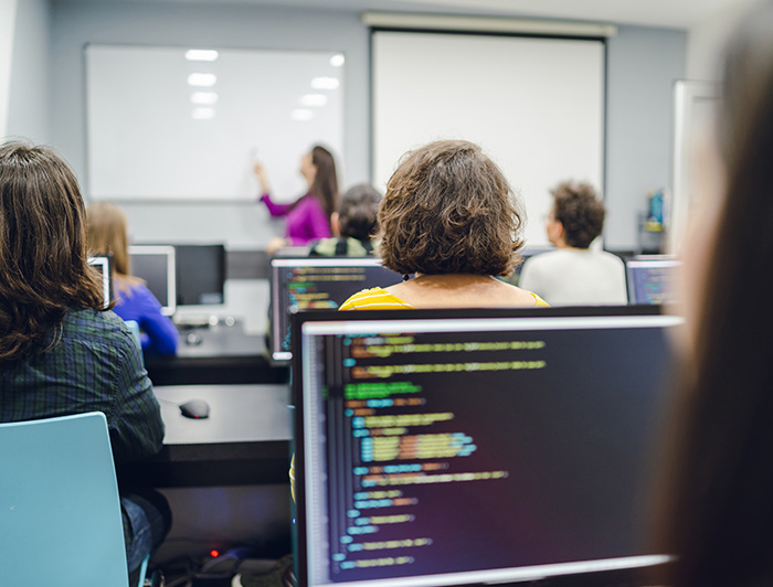 Grupo de personas sentadas frente a un computador en una sala de clases.