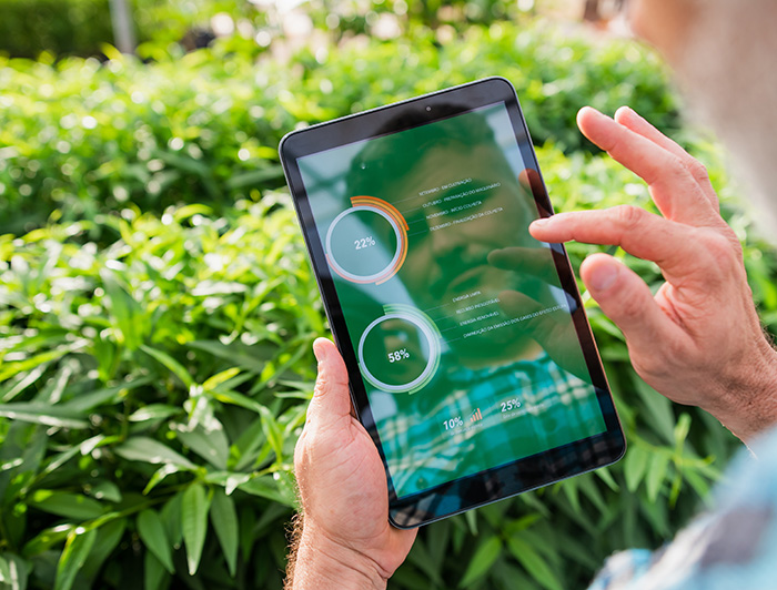 A person is monitoring data in a tablet. The background is full of green grass.