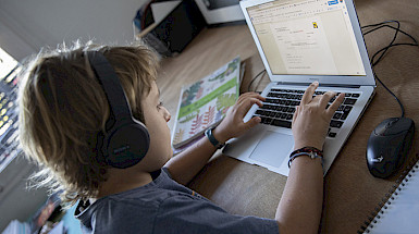Niño con audífonos escribiendo en un computador.