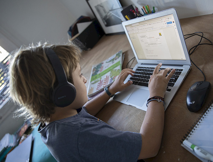 Niño con audífonos escribiendo en un computador.