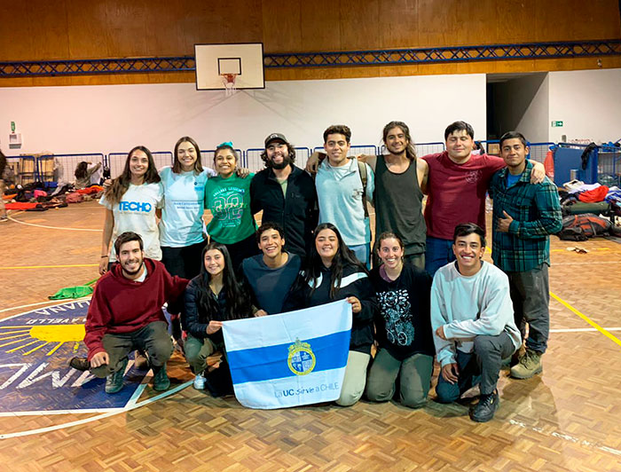 Un grupo de voluntarios por la reconstrucción post incendios sosteniendo una bandera de la UC Sirve a Chile en un gimnasio.
