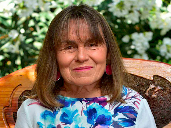 Fotografía de perfil de Patricia May con un respaldo de madera y vegetación de fondo