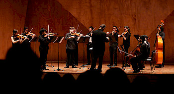 Orquesta tocando en un escenario con siluetas de público