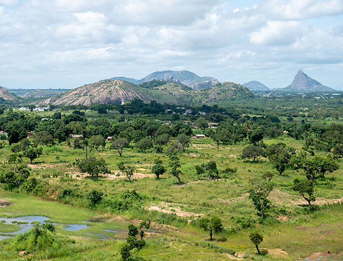 Paisaje de Mozambique de pastos y árboles, con montañas de fondo, muy verde. 