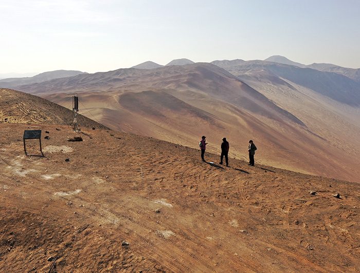 Personas se encuentran de pie a lo lejos en medio del desierto y un instrumento de medición a un costado.