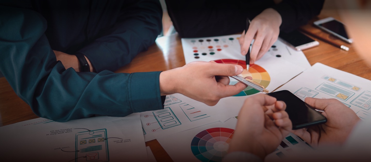 Personas reunidas en una mesa de trabajo viéndose solo sus manos, lápices y gráficos