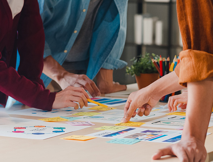 Personas trabajan en equipo, se ve solo sus brazos y manos, lápices, papeles y post it.