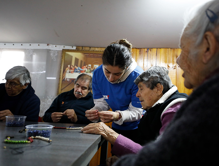 Una joven voluntaria realiza una actividad de tejer collares con personas mayores.