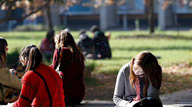 Una joven leyendo en el patio junto a otros estudiantes.