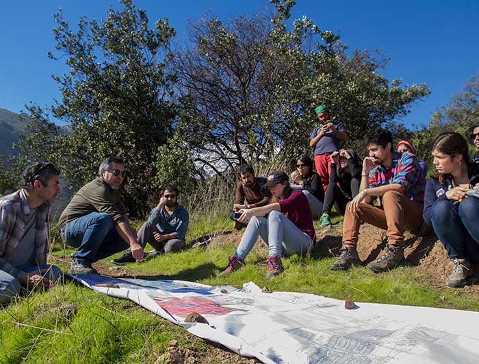 Estudiantes observan un plano sentados en el suelo, rodeados de un entorno natural. 