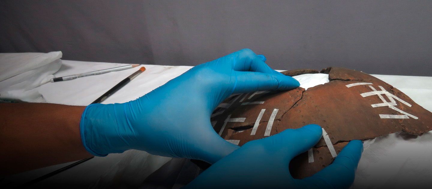 Inglés The image shows blue-gloved hands restoring an earthenware vessel.