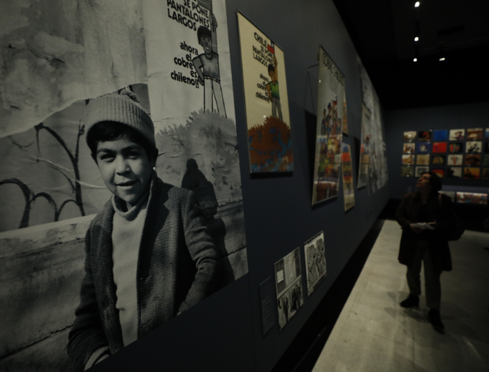 Person looking the exhibition. In the foreground there is a poster of a child with a beanie and above him it says the phrase "now copper is Chilean"