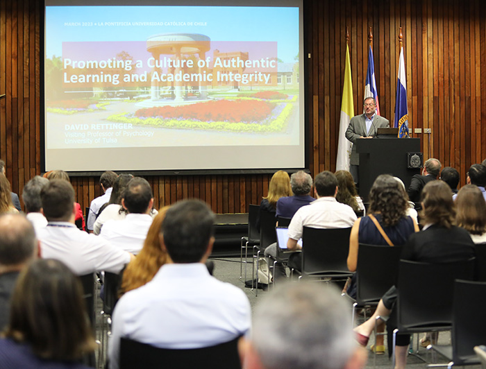 David Rettinger ofreciendo su conferencia desde un podio con su presentación proyectada y público en una sala.