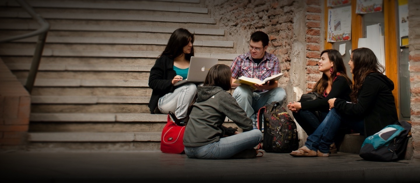 Jóvenes estudiantes están sentados en una escalera con un computador, un libro y sus mochilas.