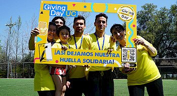 Grupo de personas usando polera amarilla y posando en un marco de Giving Day en una cancha de fútbol.