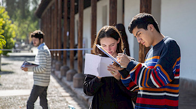Dos jóvenes, hombre y mujer, anotan en sus cuadernos de pie en un patio.