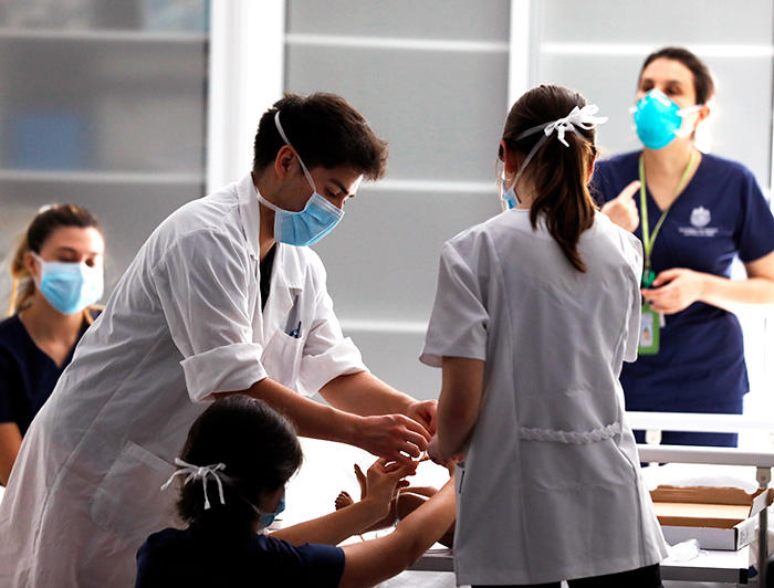 Un estudiante hombre con delantal blanco realiza una simulación junto a sus compañeras en una carrera del área de salud.