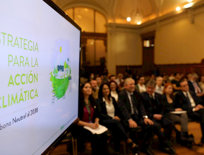 Launch ceremony of the Strategy for Climate Action in which tfuhe public and a screen with the cover of the document are visible.